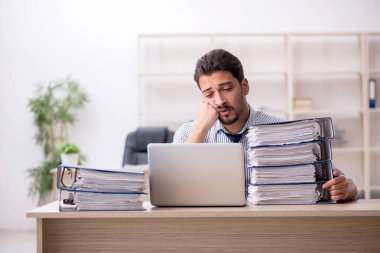 Genç bir erkek çalışan ve ofiste çok fazla iş var.