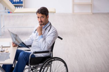 Klinikte çalışan tekerlekli sandalyedeki genç erkek doktor.