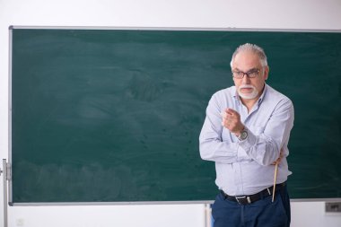 Yaşlı erkek öğretmen yeşil panonun önünde.