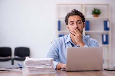 Genç bir erkek çalışan ve ofiste çok fazla iş var.