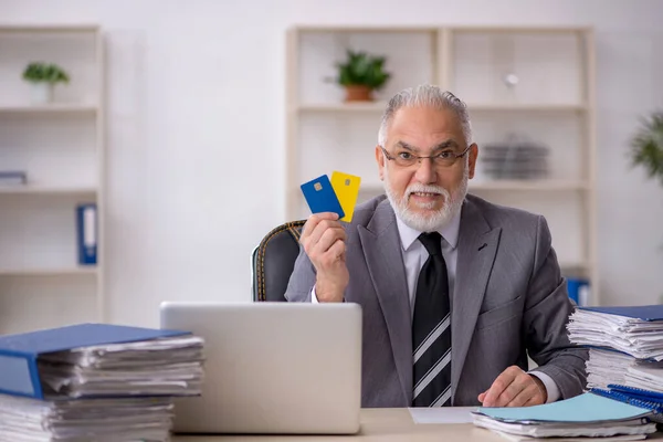 Old male employee holding credit card in the office — Stock Photo, Image