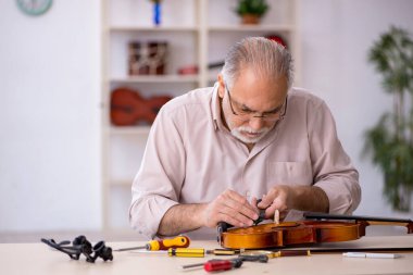 Yaşlı erkek tamirci atölyede müzik aletlerini tamir ediyor.