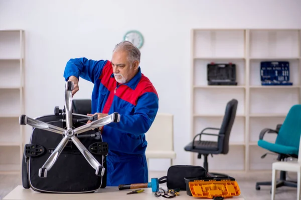 Eski erkek tamirci ofis sandalyesini tamir ediyor. — Stok fotoğraf