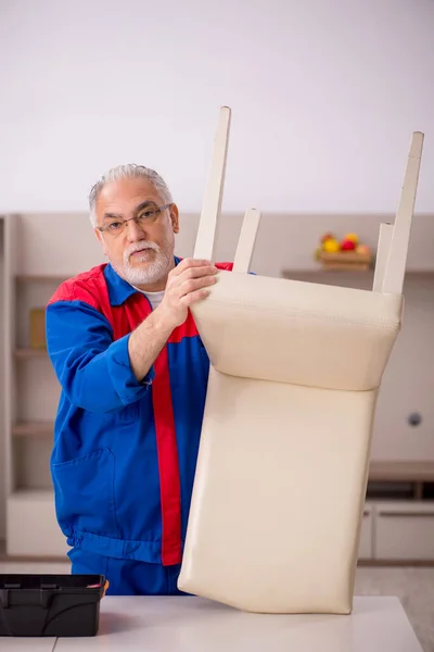 Oude mannelijke timmerman repareert stoel binnen — Stockfoto