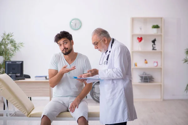 Jonge mannelijke patiënt bezoekt oude mannelijke arts — Stockfoto
