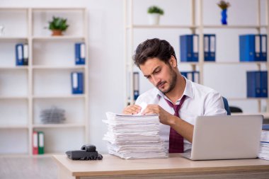 Genç bir erkek çalışan ve ofiste çok fazla iş var.