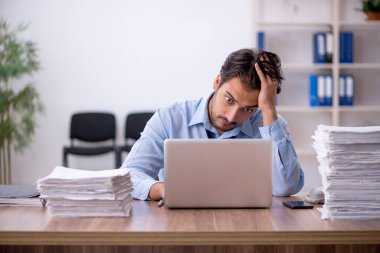 Genç bir erkek çalışan ve ofiste çok fazla iş var.