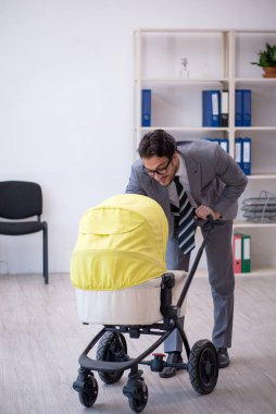 Genç erkek çalışan işyerinde yeni doğan çocuğa bakıyor.