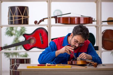 Genç adam atölyede müzik aletlerini tamir ediyor.
