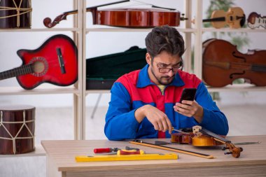 Genç adam atölyede müzik aletlerini tamir ediyor.