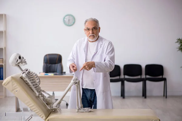 Oude mannelijke arts met skelet in de kliniek — Stockfoto