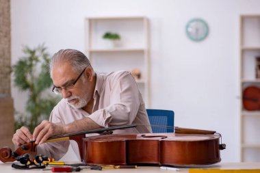 Yaşlı erkek tamirci atölyede müzik aletlerini tamir ediyor.