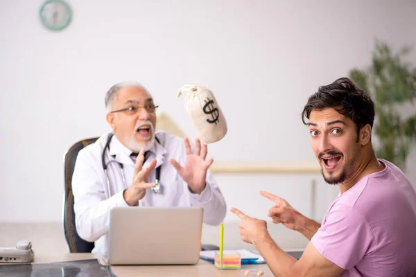 Mladý mužský pacient navštíví starého mužského lékaře v odměňování conc — Stock fotografie