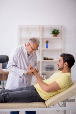 Genç hasta yaşlı doktor kayropraktik uzmanını ziyaret ediyor.