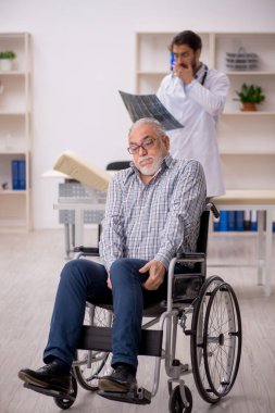 Tekerlekli sandalyedeki yaşlı adam genç doktor radyoloğu ziyaret ediyor.