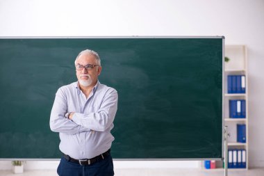 Eski öğretmen yeşil panonun önünde.