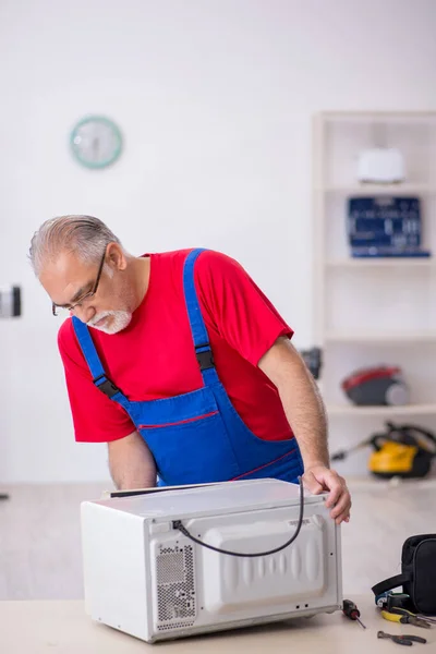 Old male repairman repairing oven at workshop