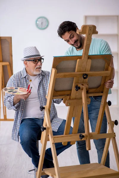 Old male painter teaching young male student at studio