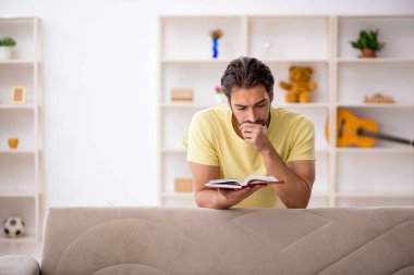 Genç erkek öğrenci salgın sırasında evde kitap okuyor.