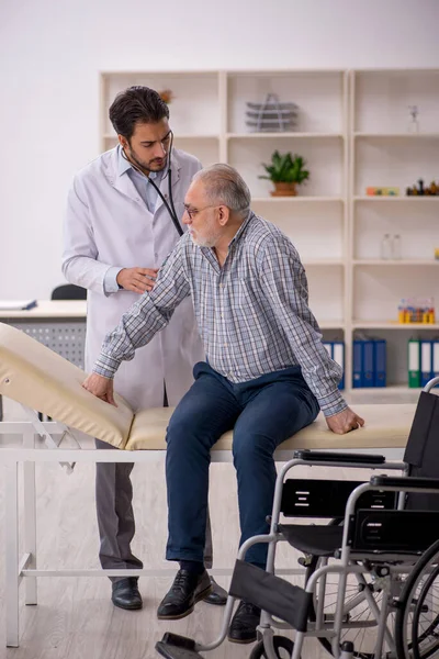 Old male patient in wheelchair visiting young male doctor