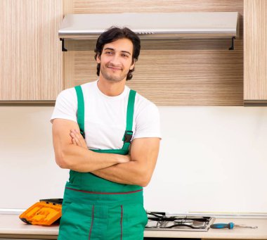 Genç müteahhit mutfakta fırın onarıyor.