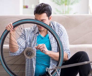 Genç adam evde bisiklet tamir ediyor.