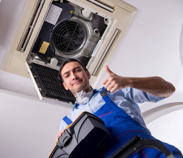 Молодой ремонтник ремонтирует потолочный кондиционер