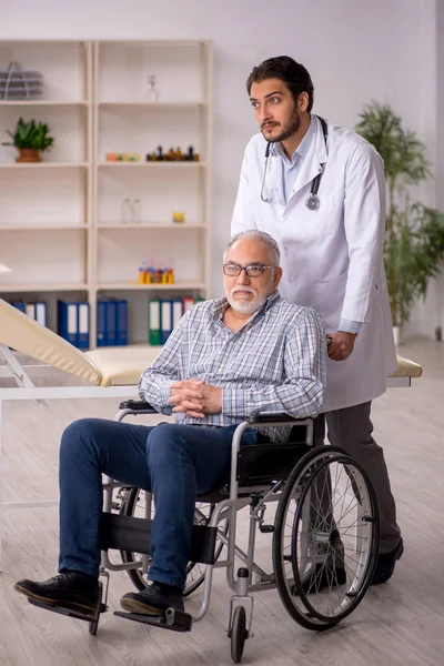 Old male patient in wheelchair visiting young male doctor