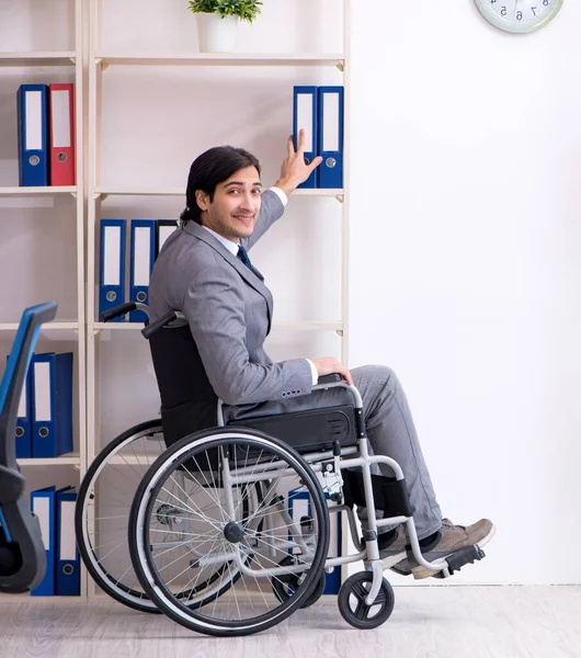 The young handsome employee in wheelchair working in the office