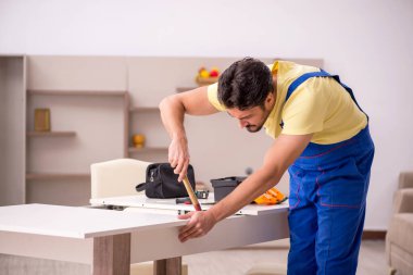 Genç marangoz evdeki masayı onarıyor.