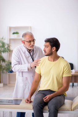 Genç hasta yaşlı erkek doktoru ziyaret ediyor.