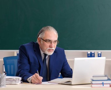 Tahtanın önündeki yaşlı erkek öğretmen.