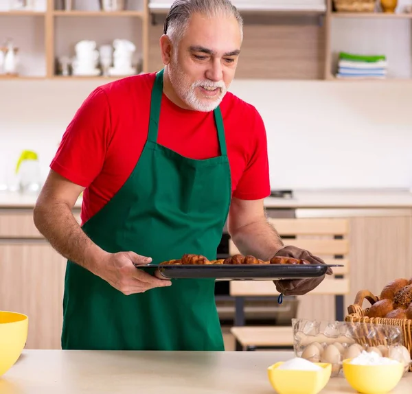 The old male baker working in the kitchen