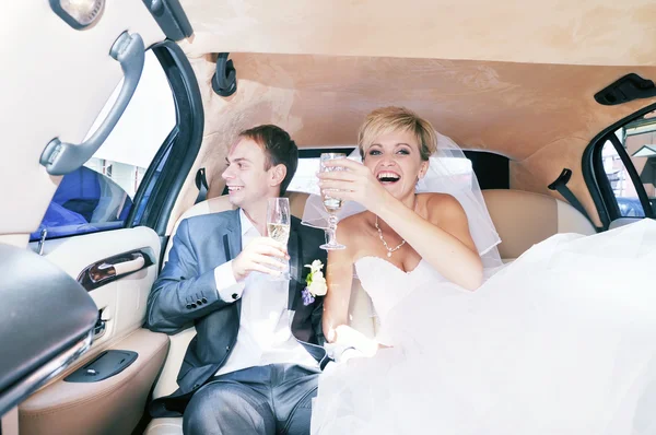 Jeunes mariés buvant du champagne dans leur limousine — Photo