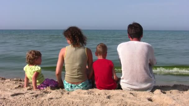 Detrás de la familia de cuatro sentados en la playa — Vídeo de stock