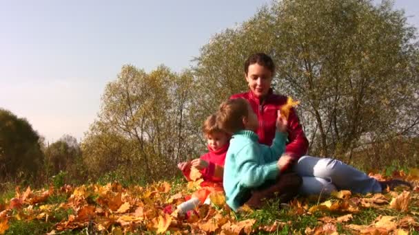 Moeder met kinderen zitten in de herfst bladeren. — Stockvideo