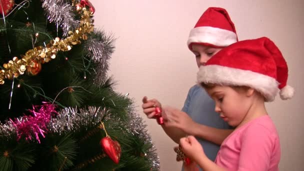 I bambini con cappelli rossi appendono il giocattolo di albero di pelo su albero di Natale — Video Stock