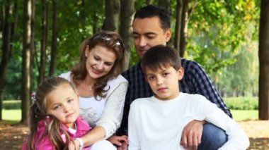 Aile ile çocuk ve kız parkta oturuyor, gülümser ve birbirlerine karşı görünüyor