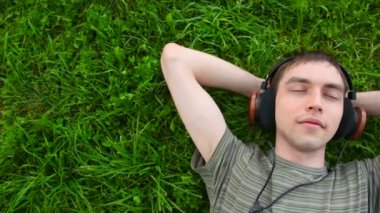 genç adam, yeşil çim üzerinde yalan, panning kulaklık müzik dinle