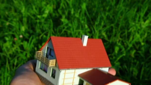 Іграшковий будинок на долоні на фоні зеленої трави — стокове відео