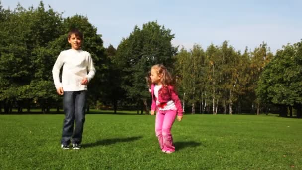 Jongen en meisje springt op veld voordat bomen — Stockvideo