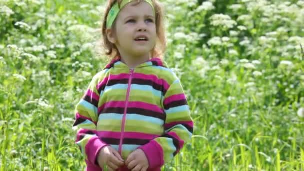 Маленькая девочка в фиолетовой блузке на зеленом поле — стоковое видео