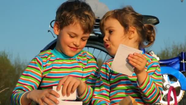 Хлопчик і дівчинка сидять на траві, дівчинка щось читає з паперу — стокове відео
