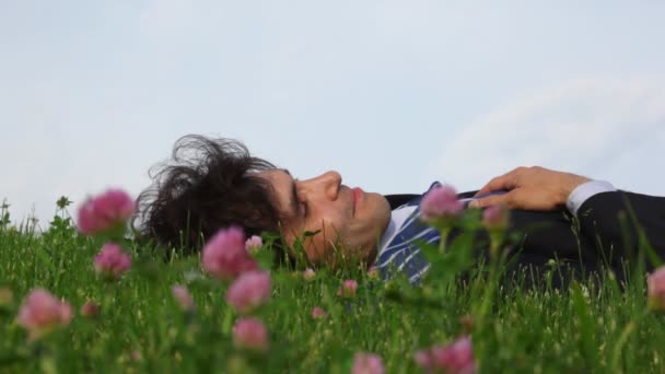 Boldog jóképű férfi feküdt a zöld fű és a virágok mező — Stock videók