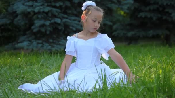 白色连衣裙的女孩坐在草地上，触动它用她的手 — 图库视频影像