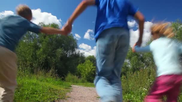Батько з сином і дочкою бігає в парку, приєднується до рук, з камери — стокове відео
