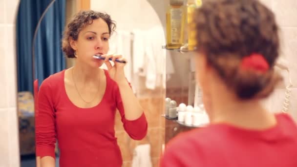 Женщина перед зеркалом чистит зубы — стоковое видео