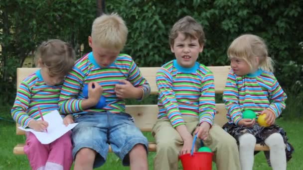 4 kinderen zittend op een bankje en spelen met ballen — Stockvideo