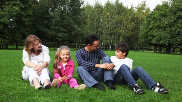 Familie mit Junge und Mädchen sitzt im Park auf Glas, blickt gegeneinander, redet und lächelt — Stockvideo