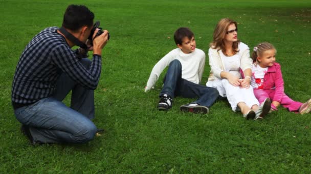 Il padre fotografa la famiglia da madre e figlia con il figlio si siede su campo in parco — Video Stock